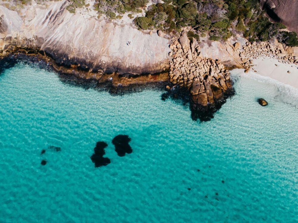 Drone shot of blue haven beach, white sand and blue water with rocks in top half of the image
