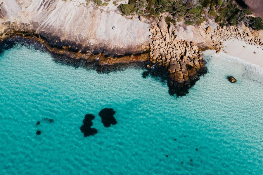 Drone shot of blue haven beach, white sand and blue water with rocks in top half of the image