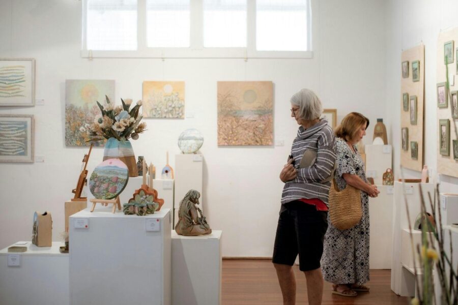 Two ladies view artworks, one small sized encaustic aqua coloured drawings, another views pottery