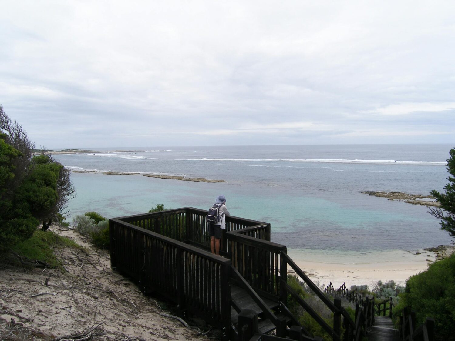 Person standing on a wooden lookout overlooking the ocean.